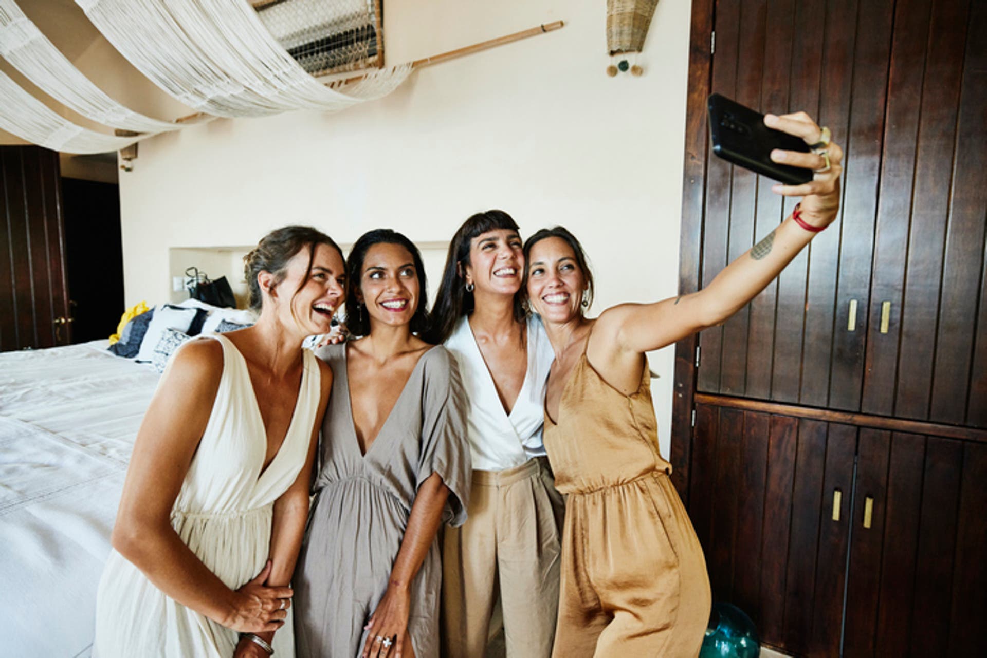  Medium wide shot of smiling and laughing bridesmaids taking selfie in luxury hotel suite 