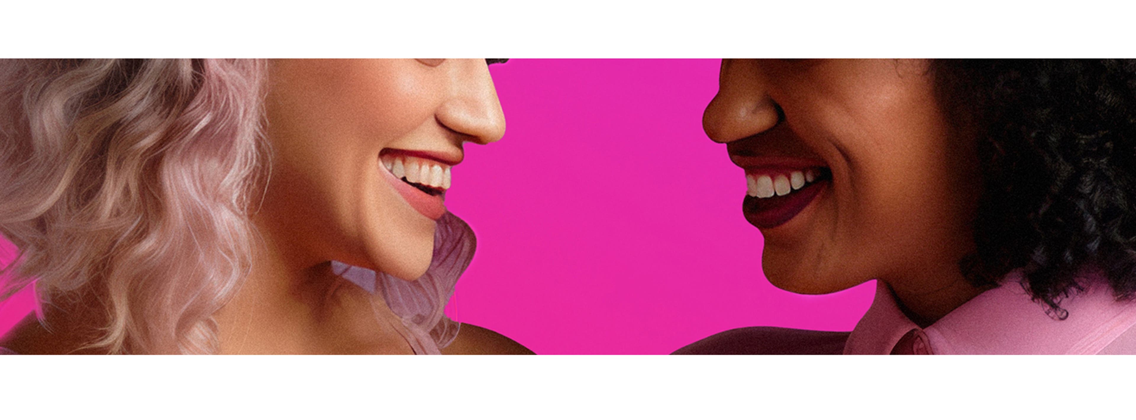 Two women wearing pink looking at each other laughing while posing for a picture