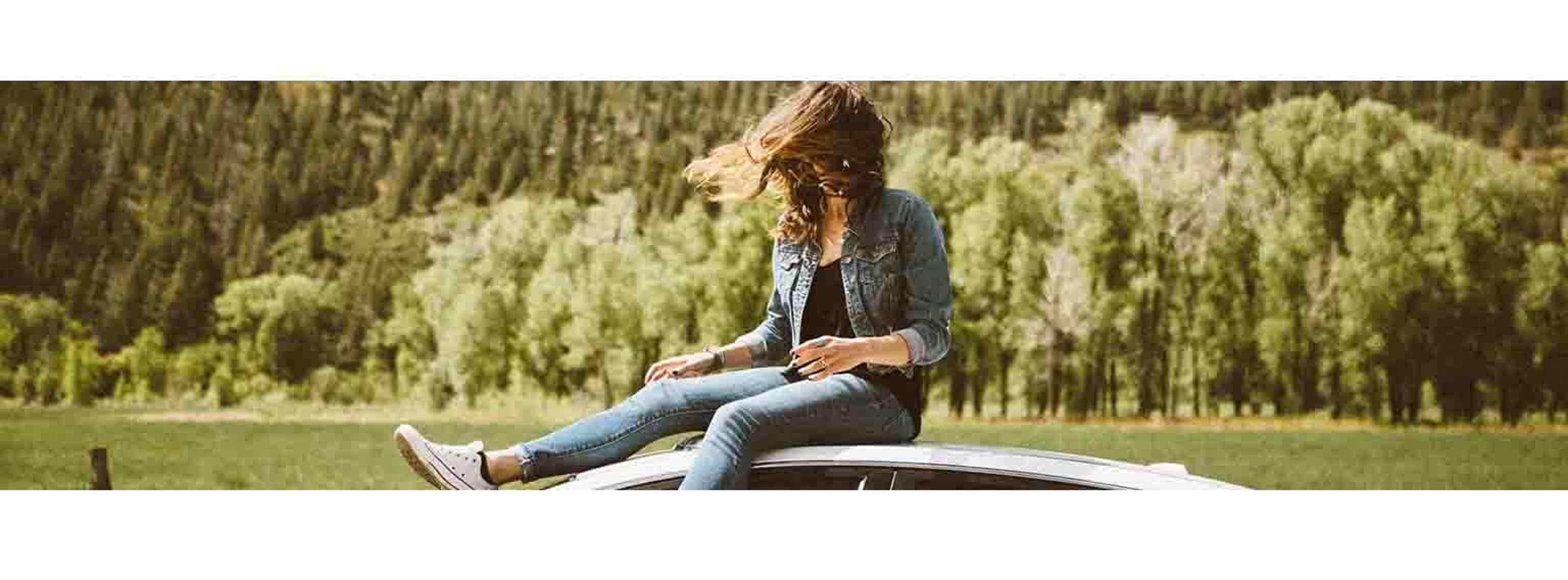 woman sitting on top of a car on a windy day