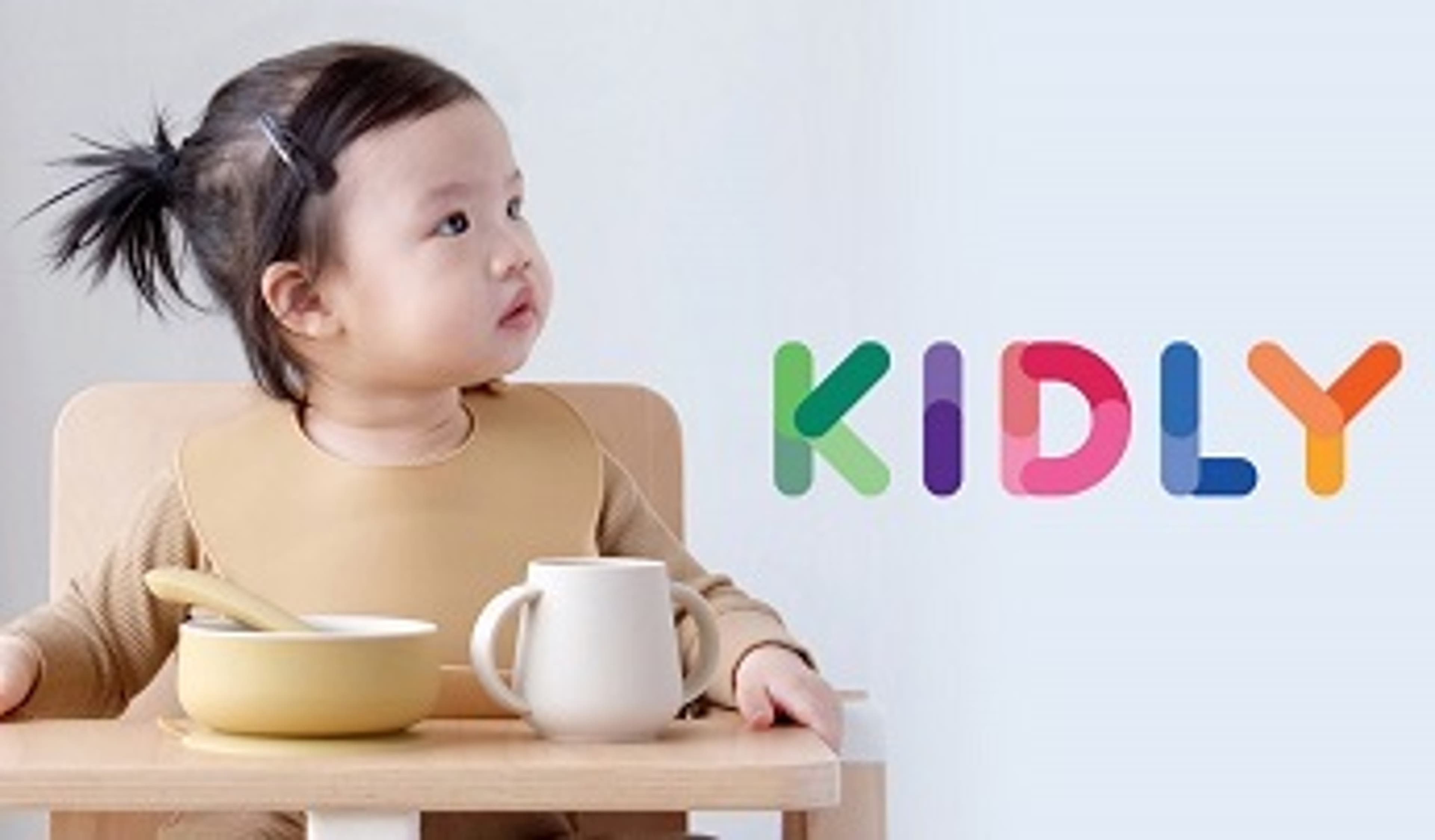  A baby sat in a highchair next to the KIDLY logo 