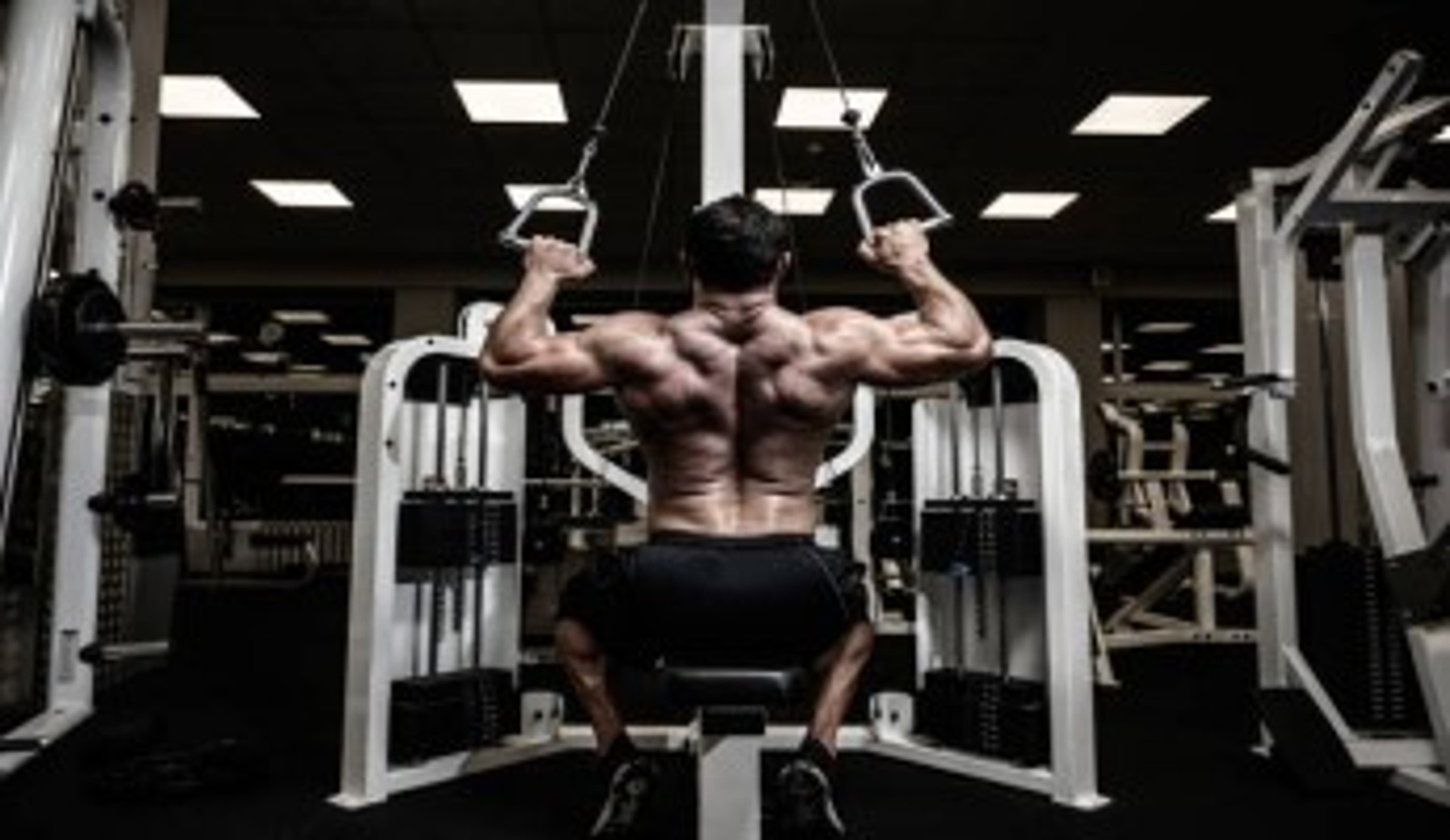  Man using lateral pull down machine at gym. 