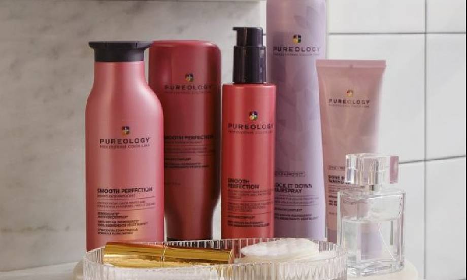 An array of Pureology haircare products in pink and purple bottles in front of a tiled bathroom wall.