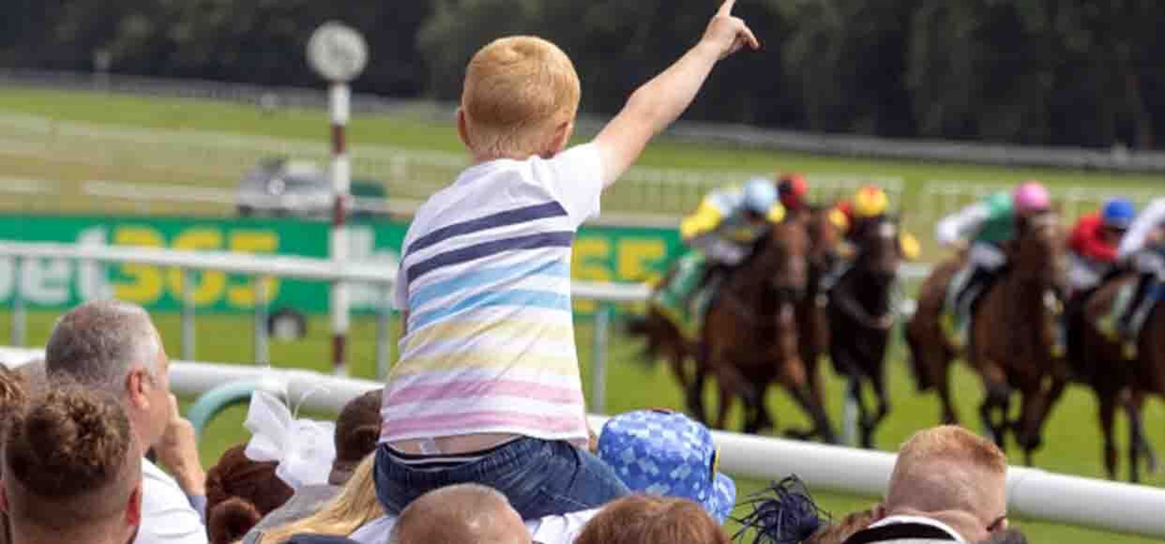 a little boy sitting on fathers shoulders pointing up looking at the races