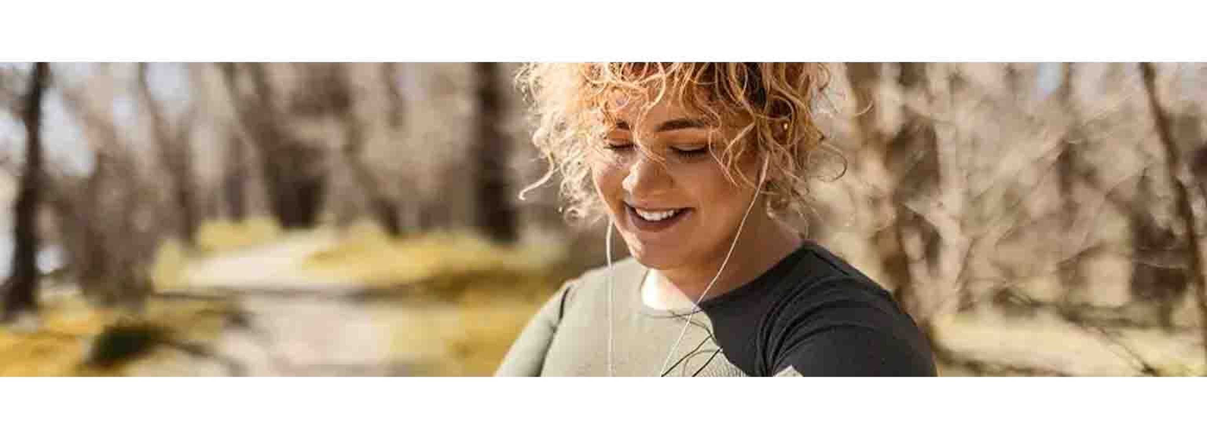 curly haired woman looking down at her watch mid run