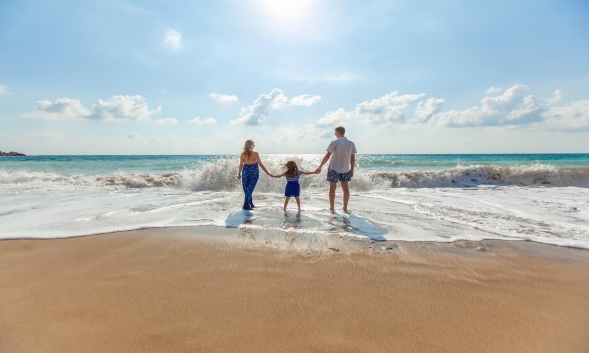  man, woman and young child paddling in shallow water on a sunny beach 