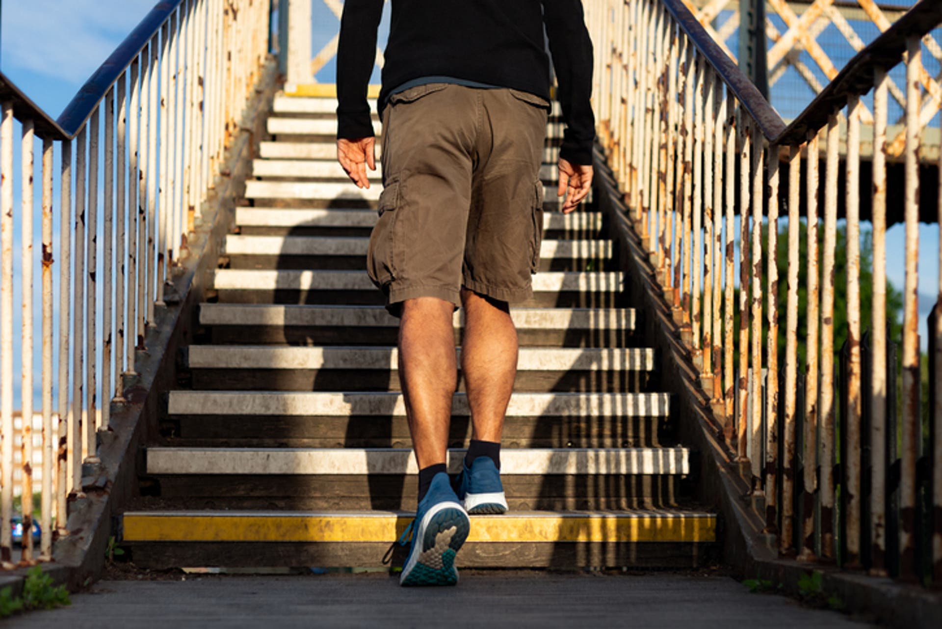  Rearview of a man wearing chino shorts climbing up the stairs of a footbridge 