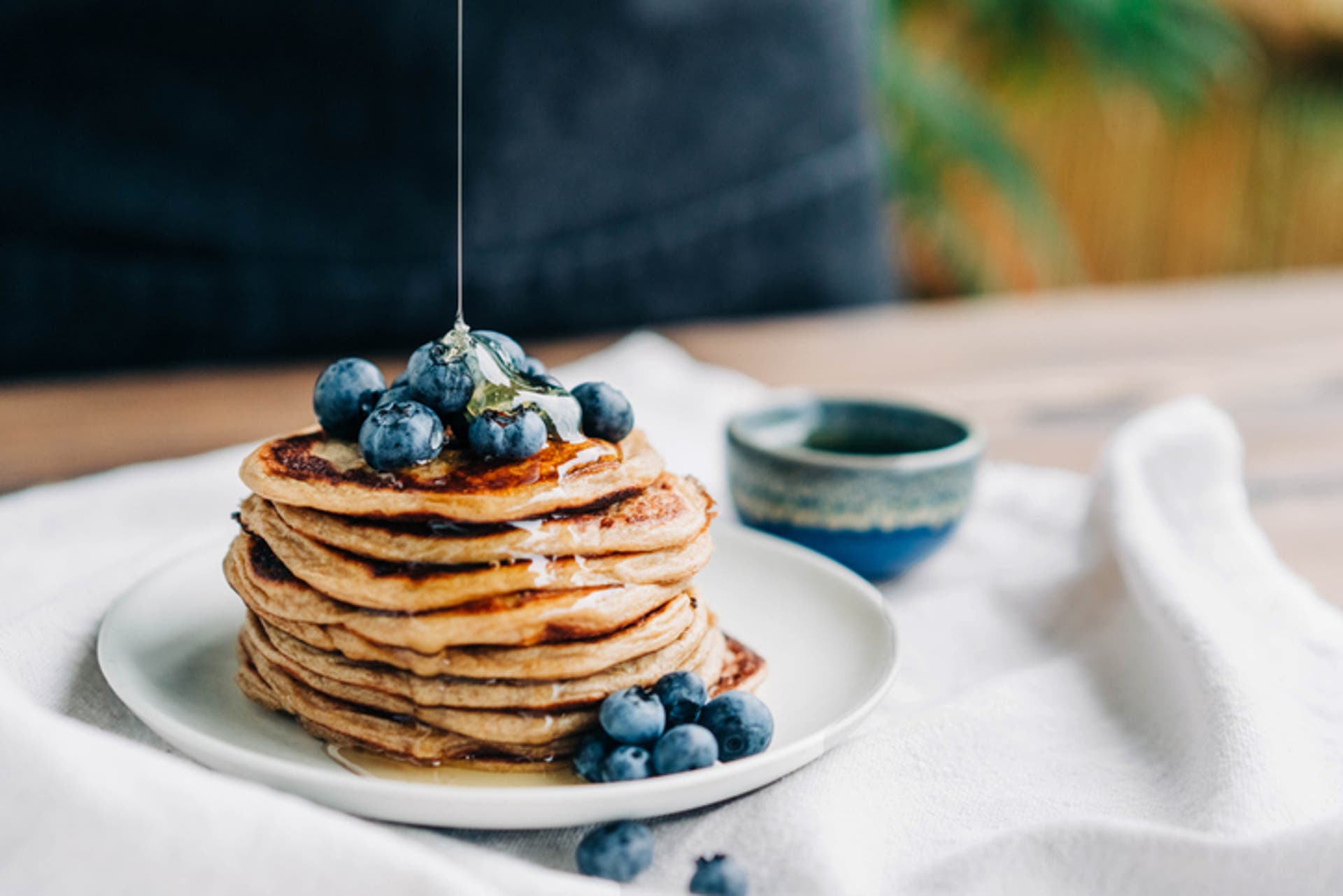  A stack of pancakes covered with syrup served on a plate with blueberries and honey. 