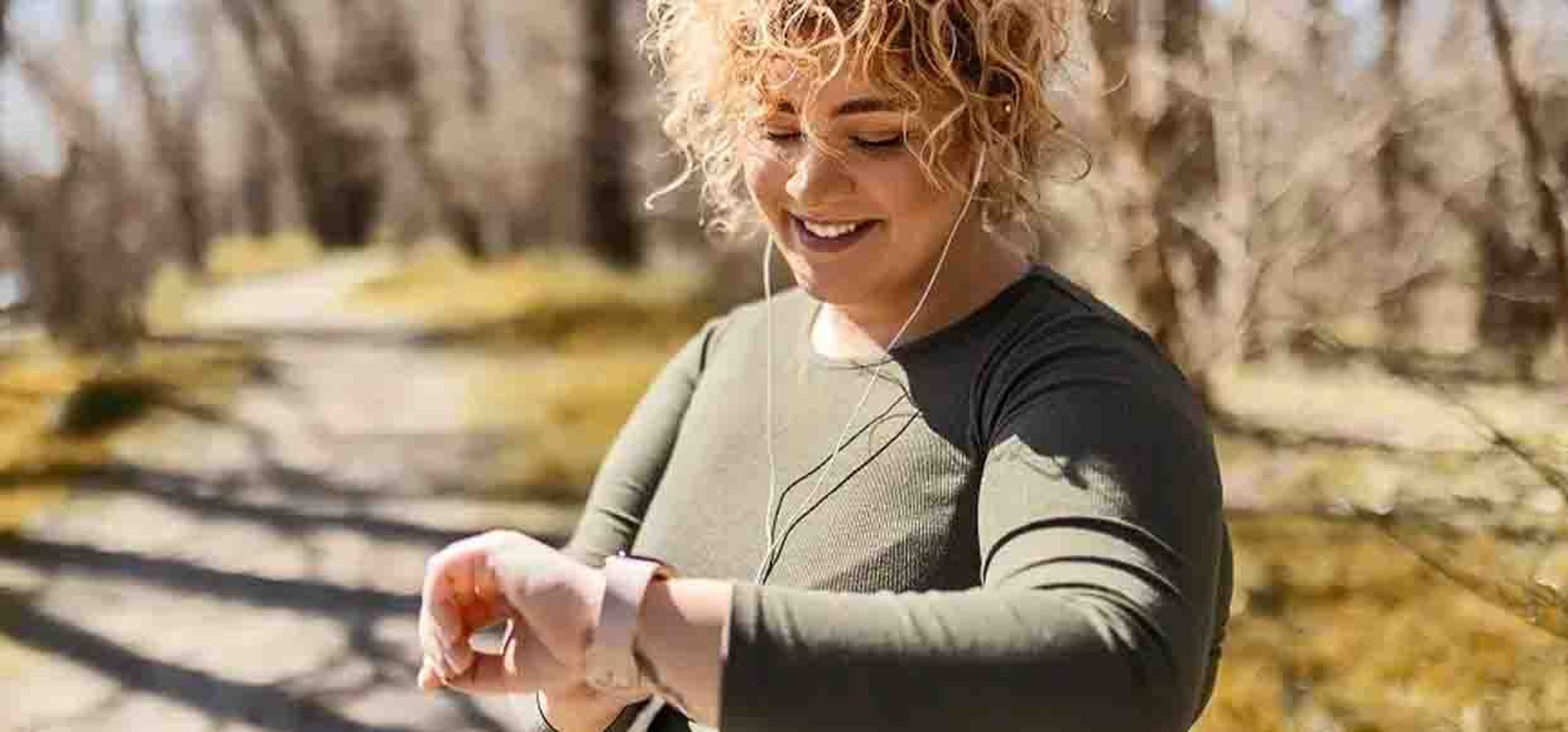 curly haired woman looking down at her watch mid run