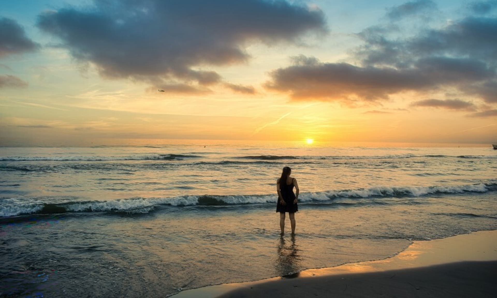  woman wearing a dress stood in the shallows of the sea at sunset 
