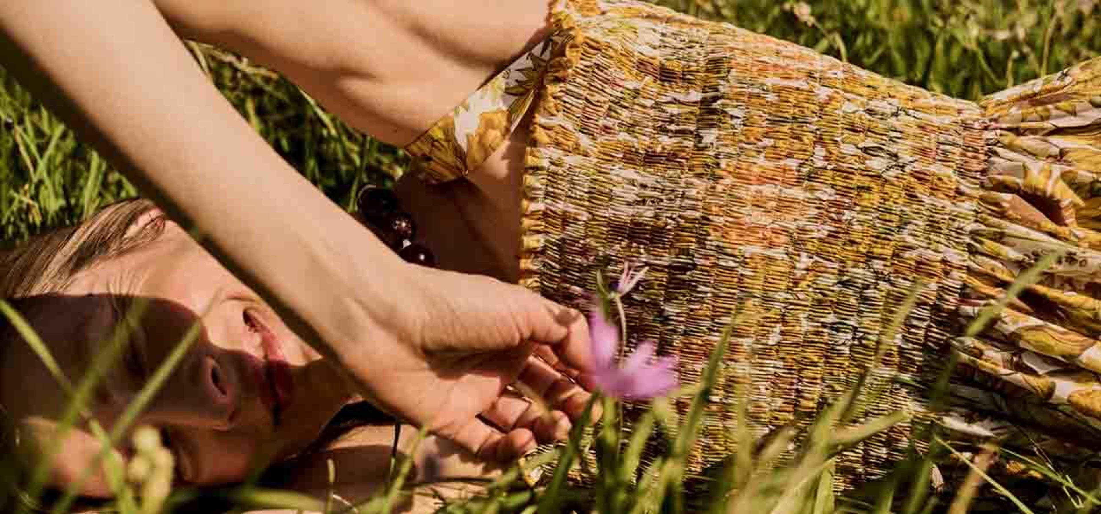 woman posing with a flower to her face laying down on a grass, close up shot