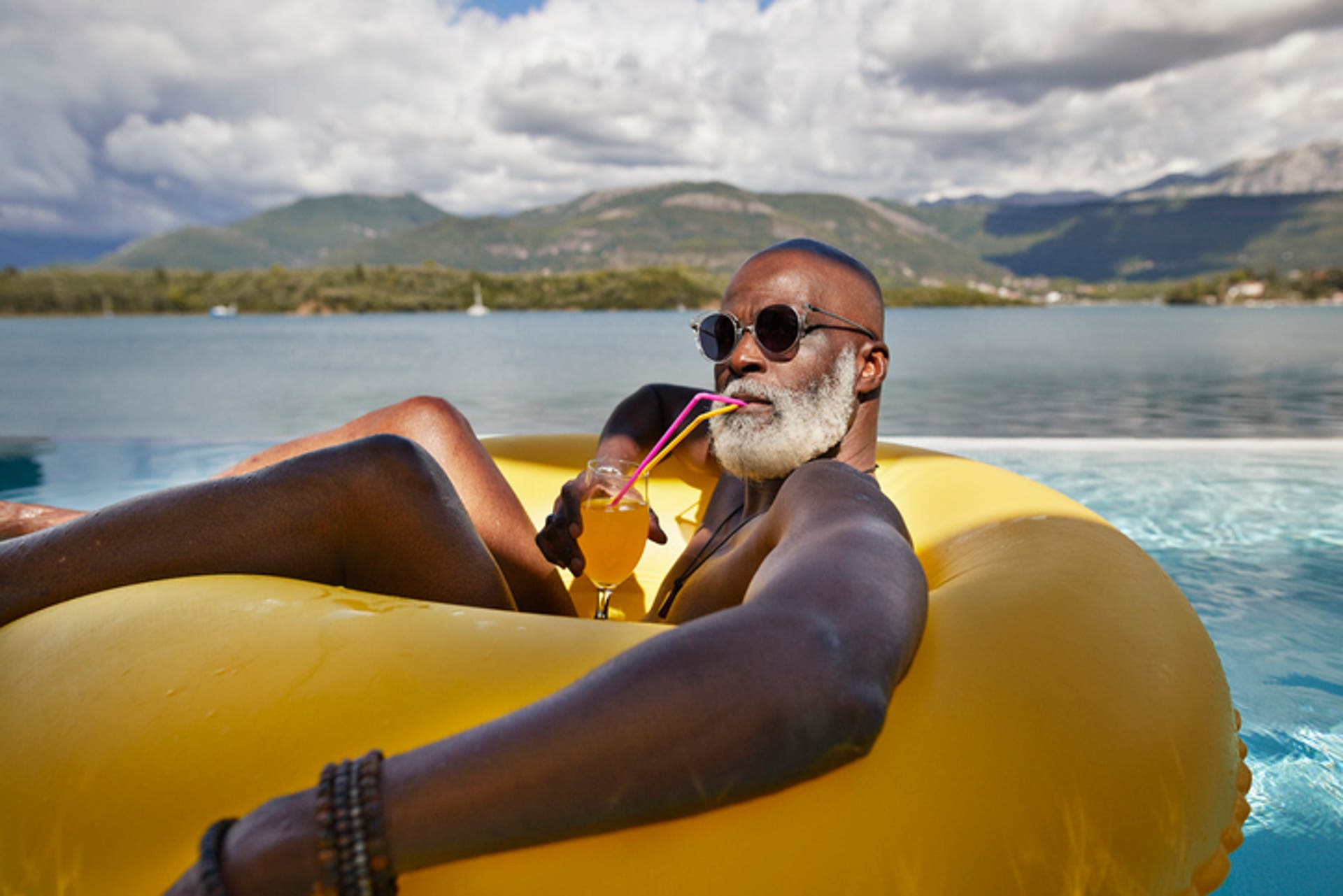  Senior man wearing sunglasses while drinking juice in inflatable ring during vacation 