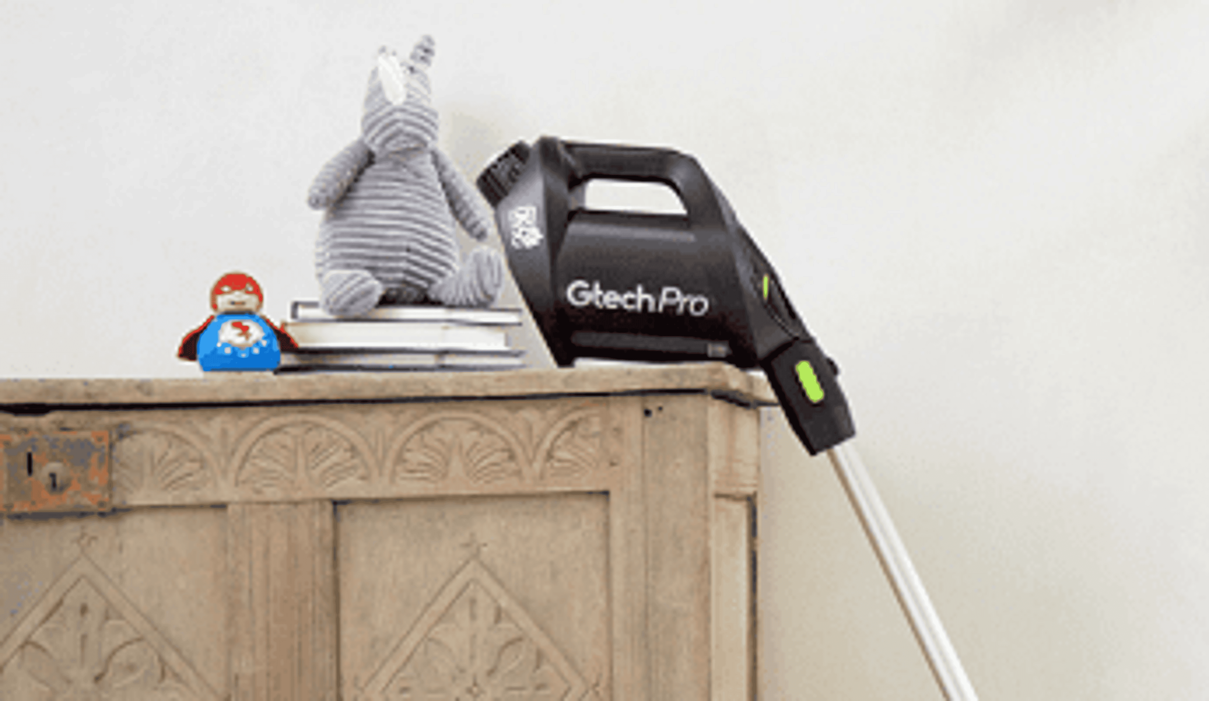  A Gtech stick vacuum resting against a wooden sideboard 