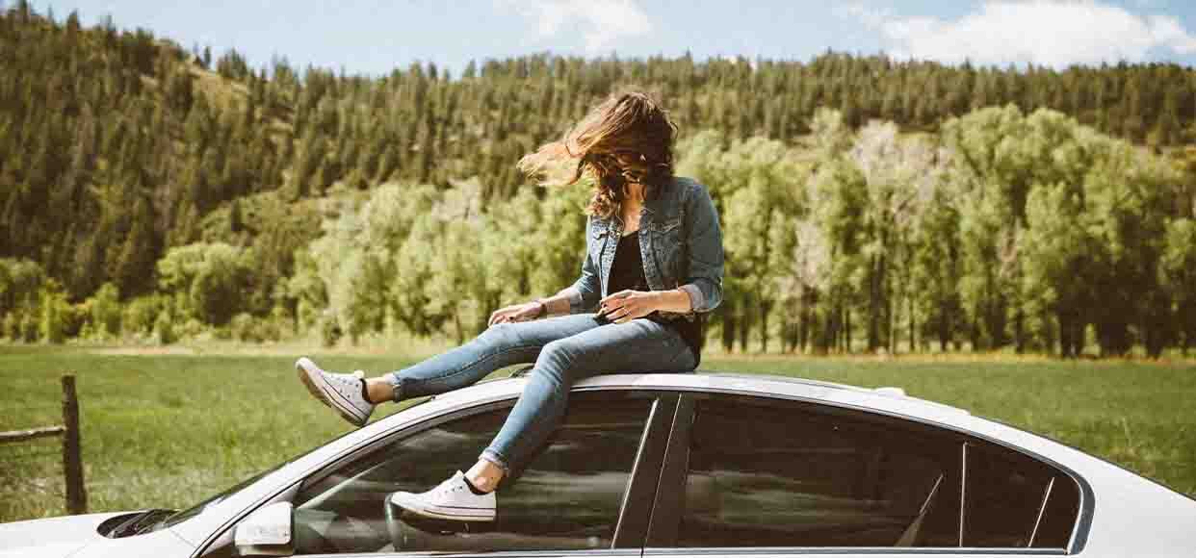 woman sitting on top of a car on a windy day