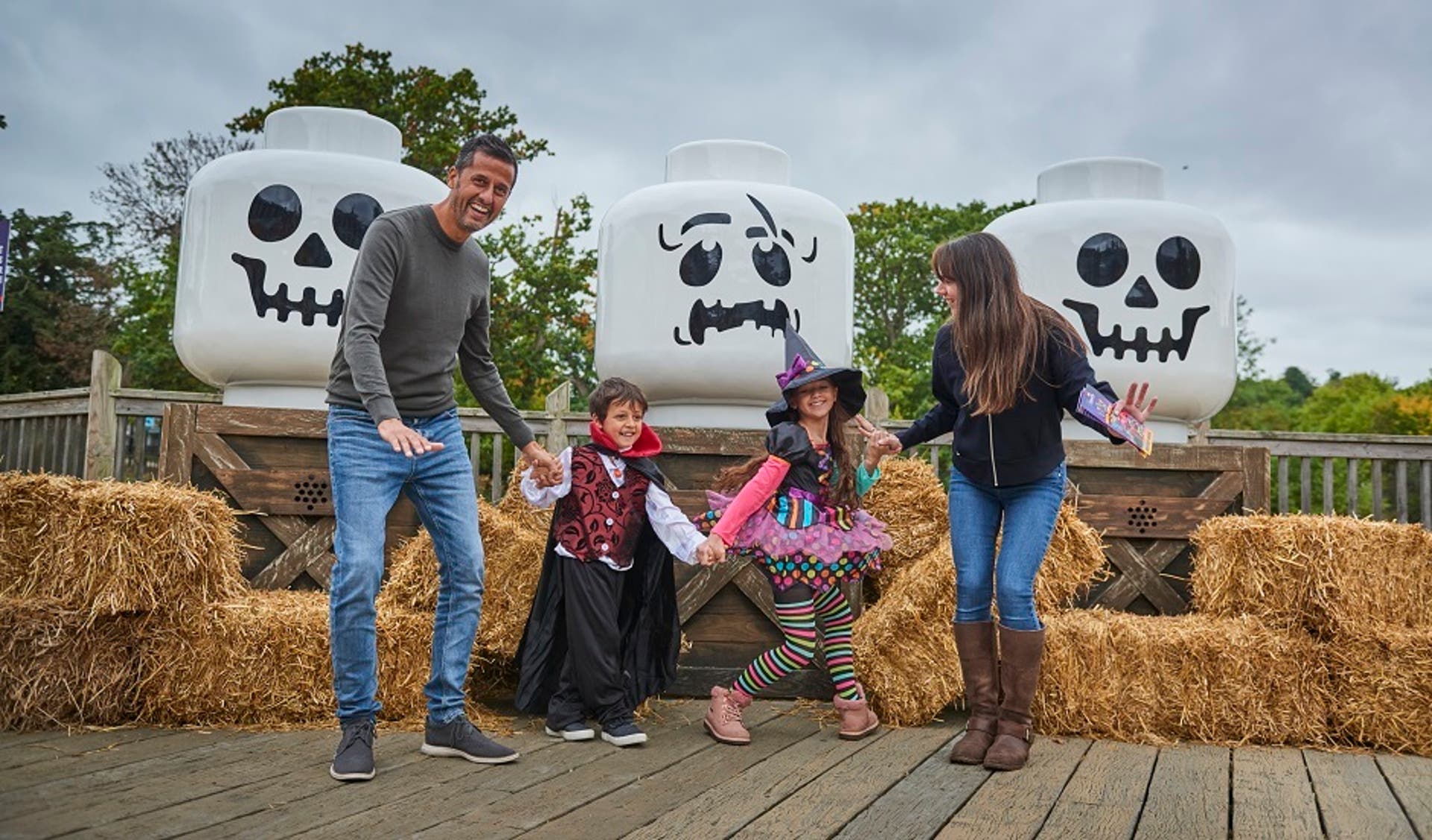  A family of four with the children in Halloween costumes stood in front of straw bales and giant Lego skulls at the Legoland Brick or Treat event. 